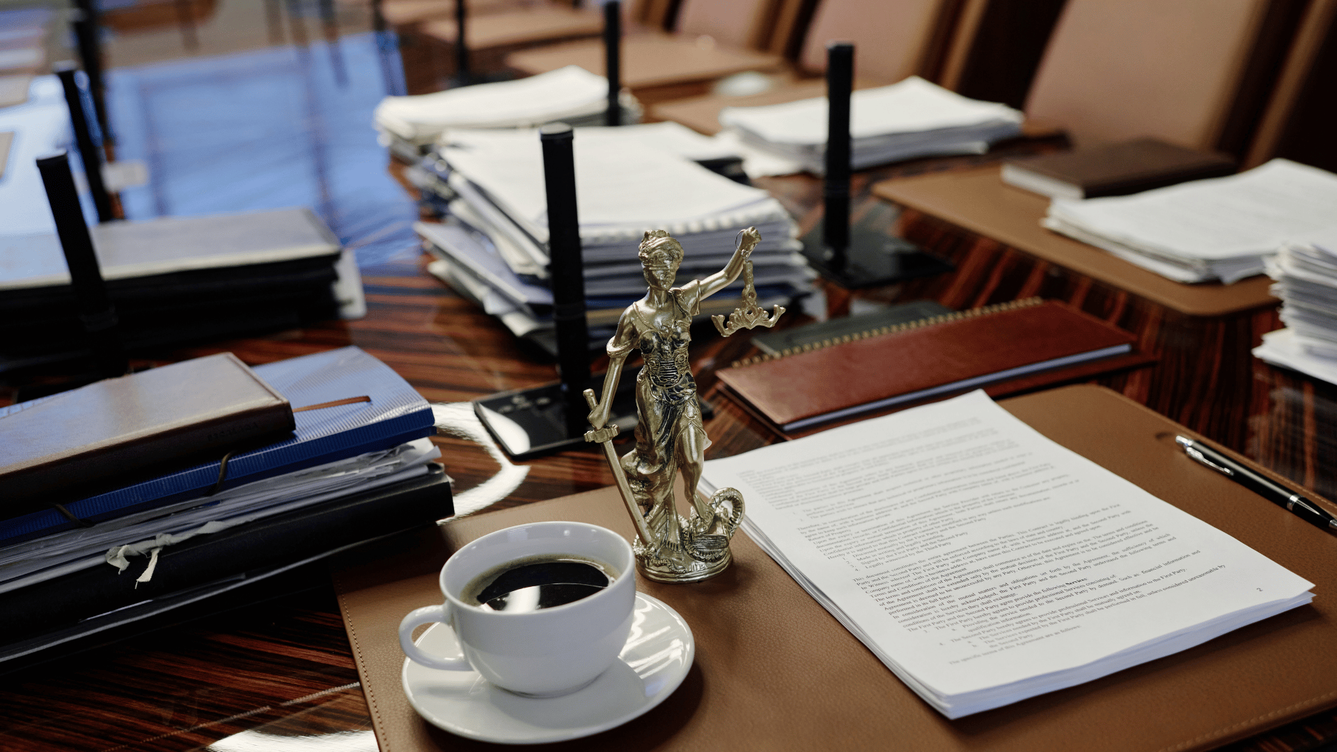Legal documents and employment compliance paperwork on a conference table with Lady Justice statue and coffee cup in the office